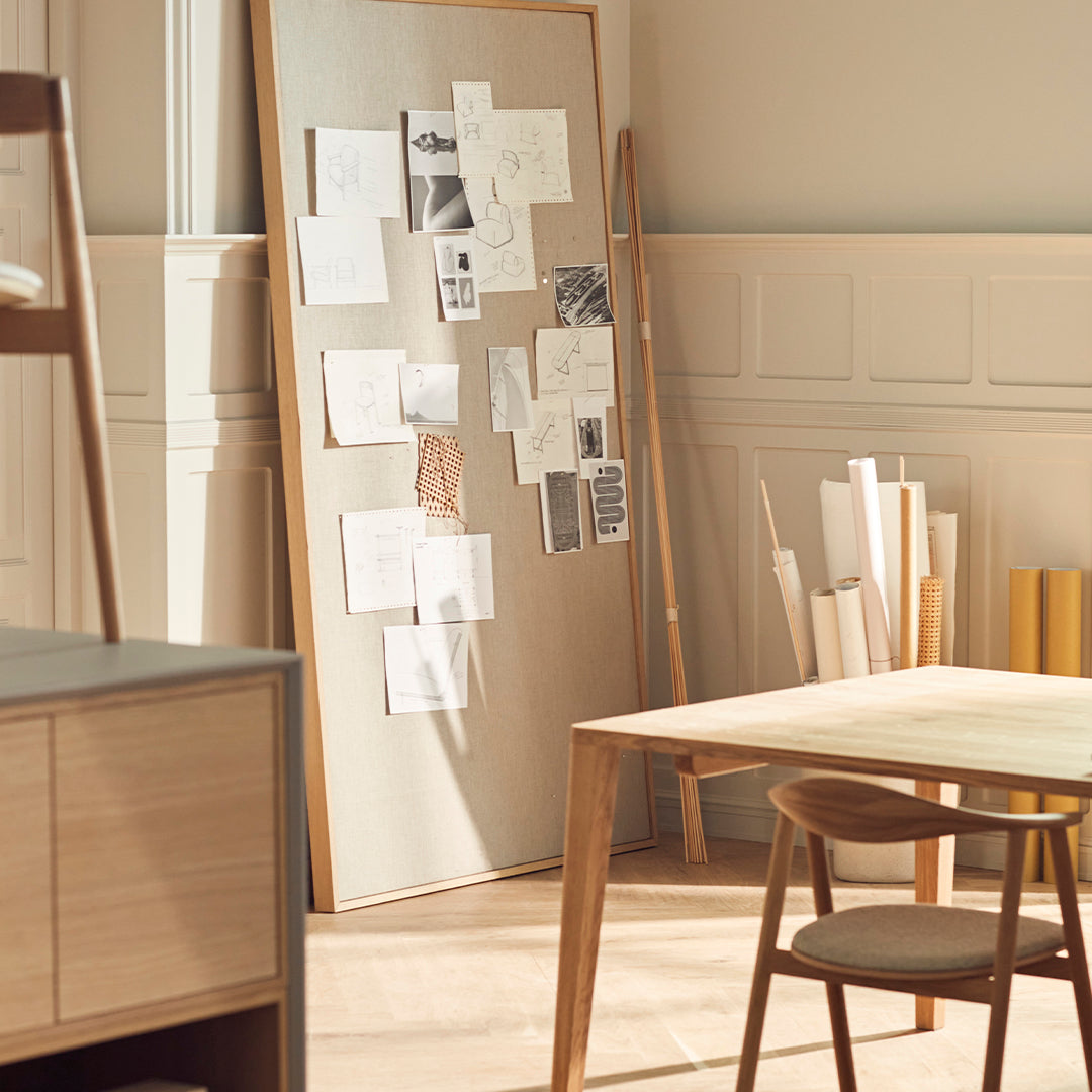 Light wooden table, beige wall board with white and black papers, warm sunlight creating a cozy atmosphere.