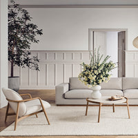 Light gray sofa with neutral tones, paired with earthy wood accents and a textured cream rug. Elegant floral arrangement.