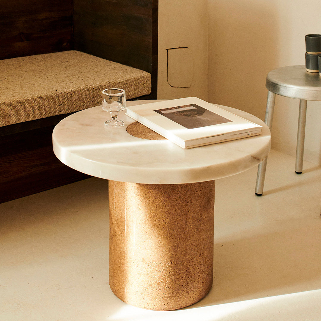 Round marble top coffee table with a textured cork base, featuring soft beige and earthy brown tones.