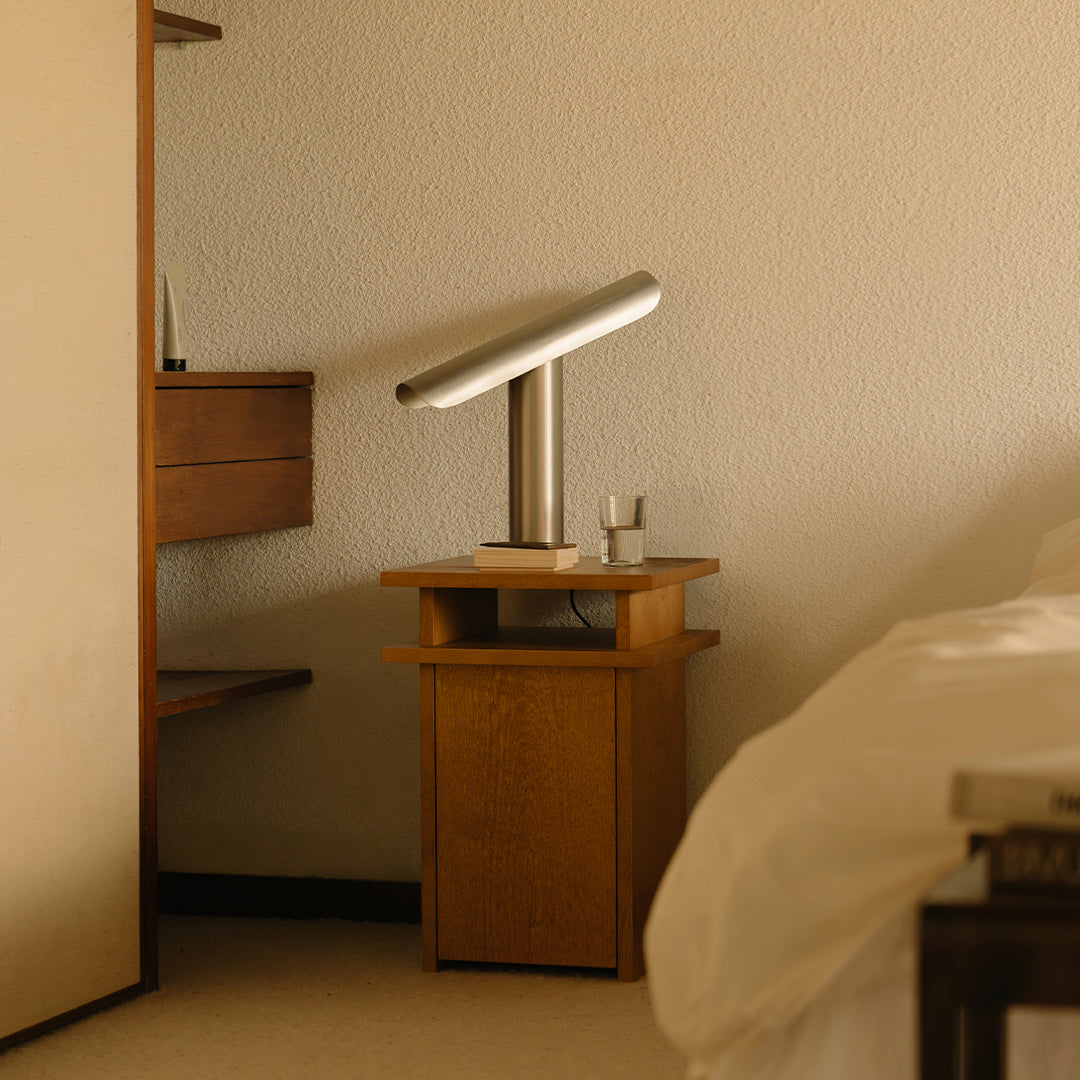 Wooden nightstand with clean lines, featuring a sleek silver lamp, set against soft beige walls and warm tones.