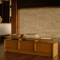 Light wooden coffee table with smooth surfaces against a textured beige brick wall. Simple, modern design.