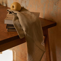 Beige linen towel draped over a wooden table, complemented by a yellow apple and stacked books.