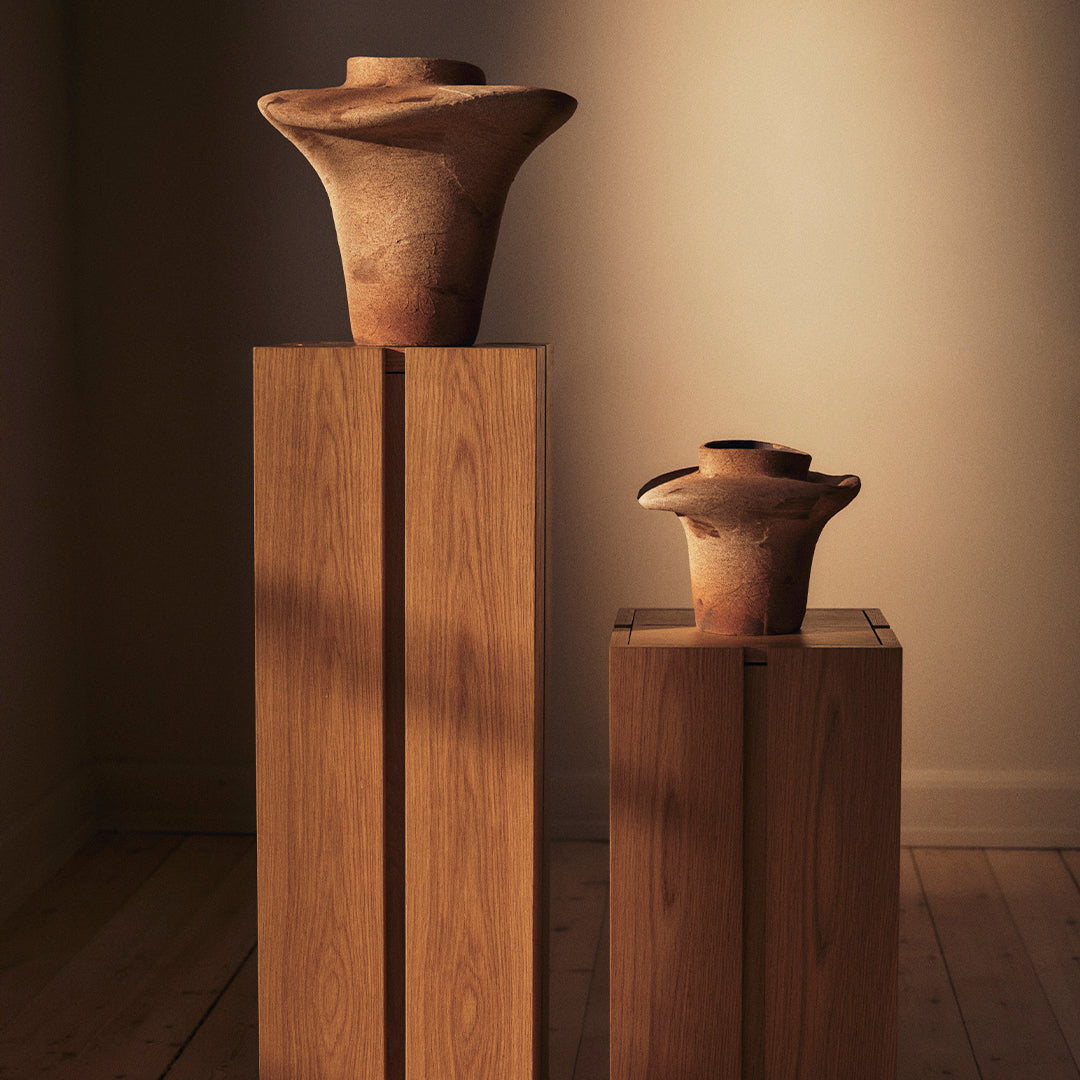"Two textured, rustic terracotta vases in earthy tones, showcasing organic shapes atop minimalist wooden pedestals."