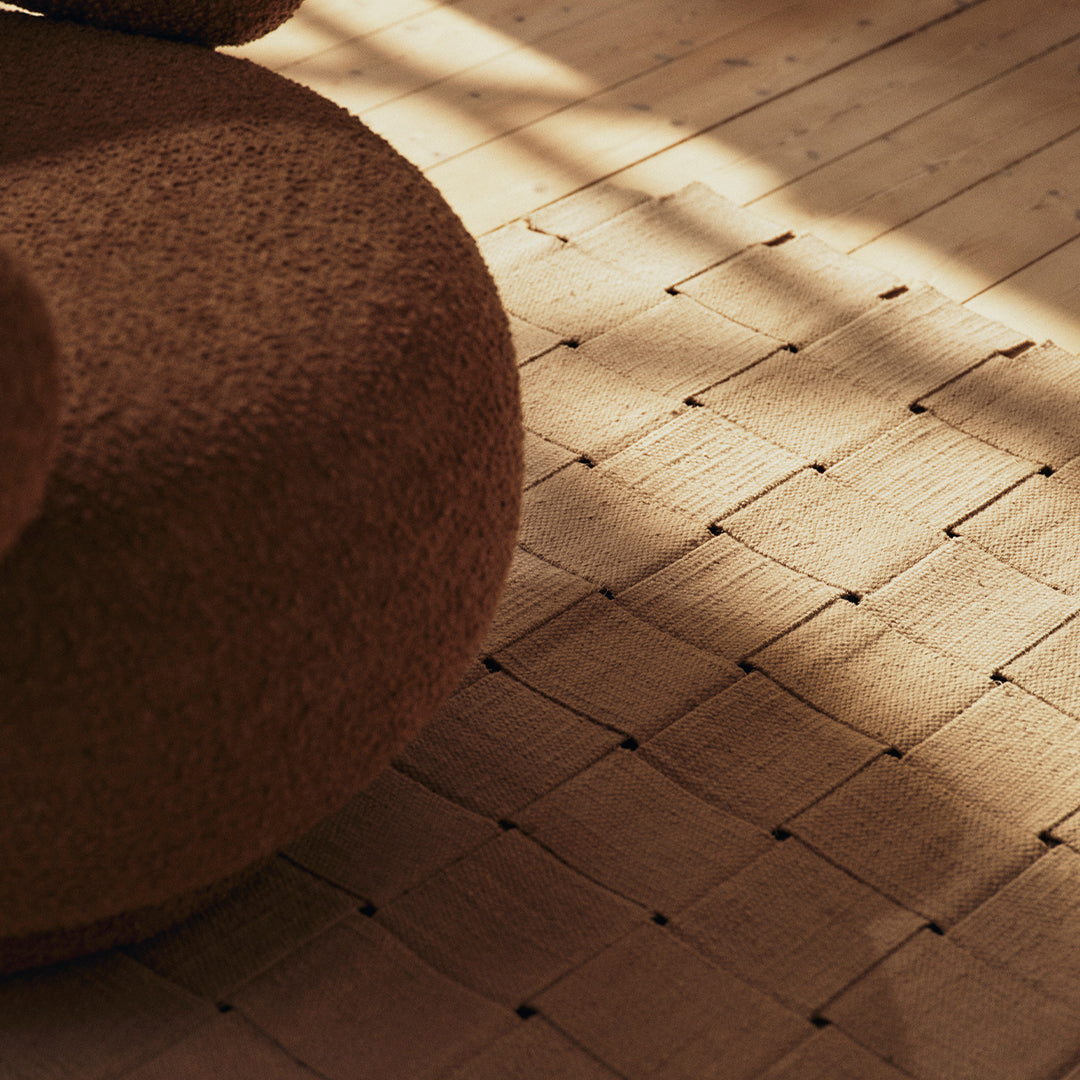 Brown textured round pouf on a patterned wooden floor with subtle light and shadow play.
