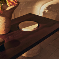 Dark wooden table with a circular stone detail, featuring soft neutral tones and subtle textures.