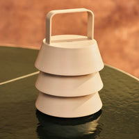 Cream-colored, tiered lantern with a handle, featuring smooth, minimalist design on a reflective green surface.