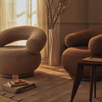 "Neutral-toned boucle chairs with soft curves, complemented by a warm, textured backdrop and natural accents."