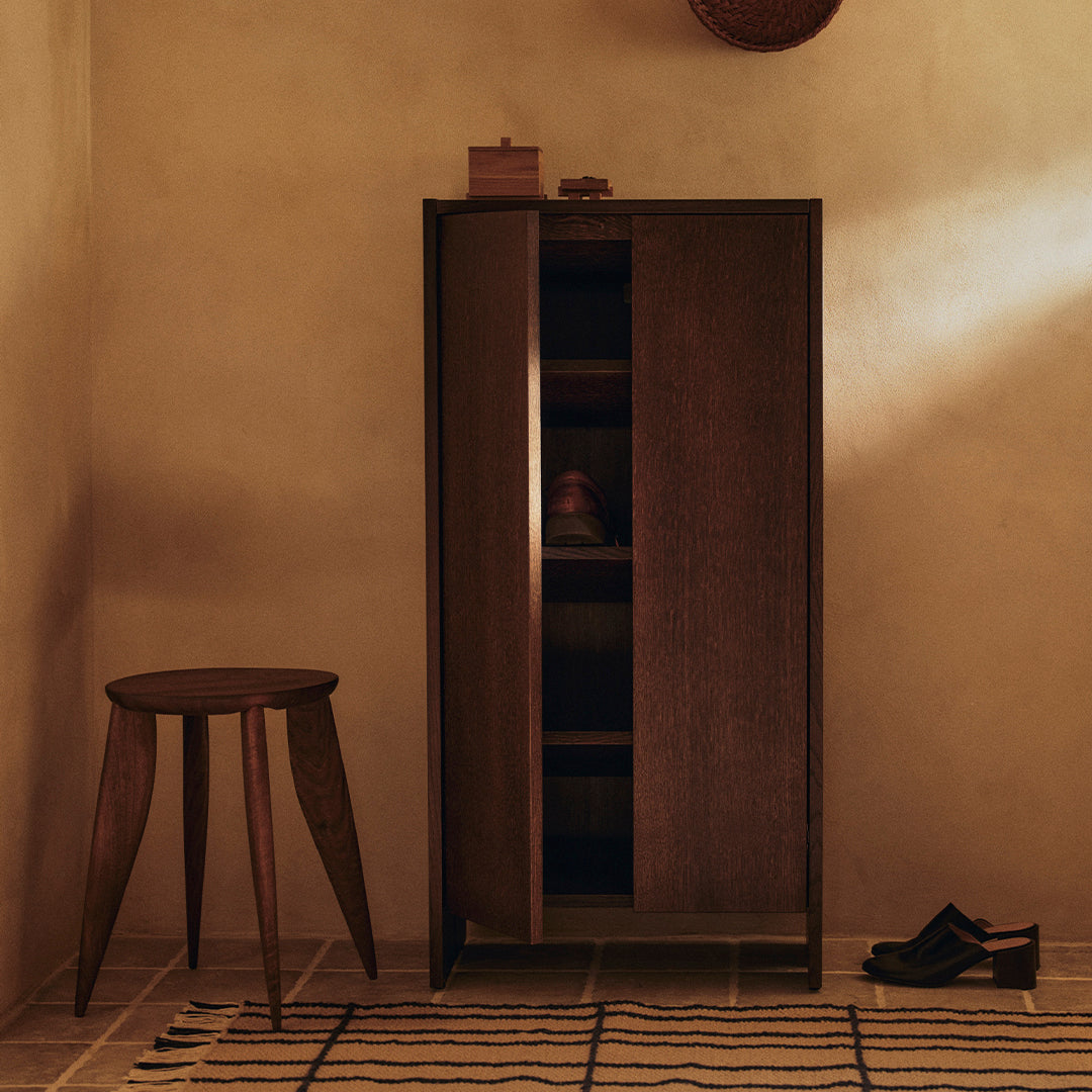 Dark wood cabinet with a minimalist design, paired with a striped beige and brown rug, in a warm-toned interior.