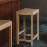 Beige wooden bar stool with a minimalist design, featuring clean lines and a smooth, simple finish.