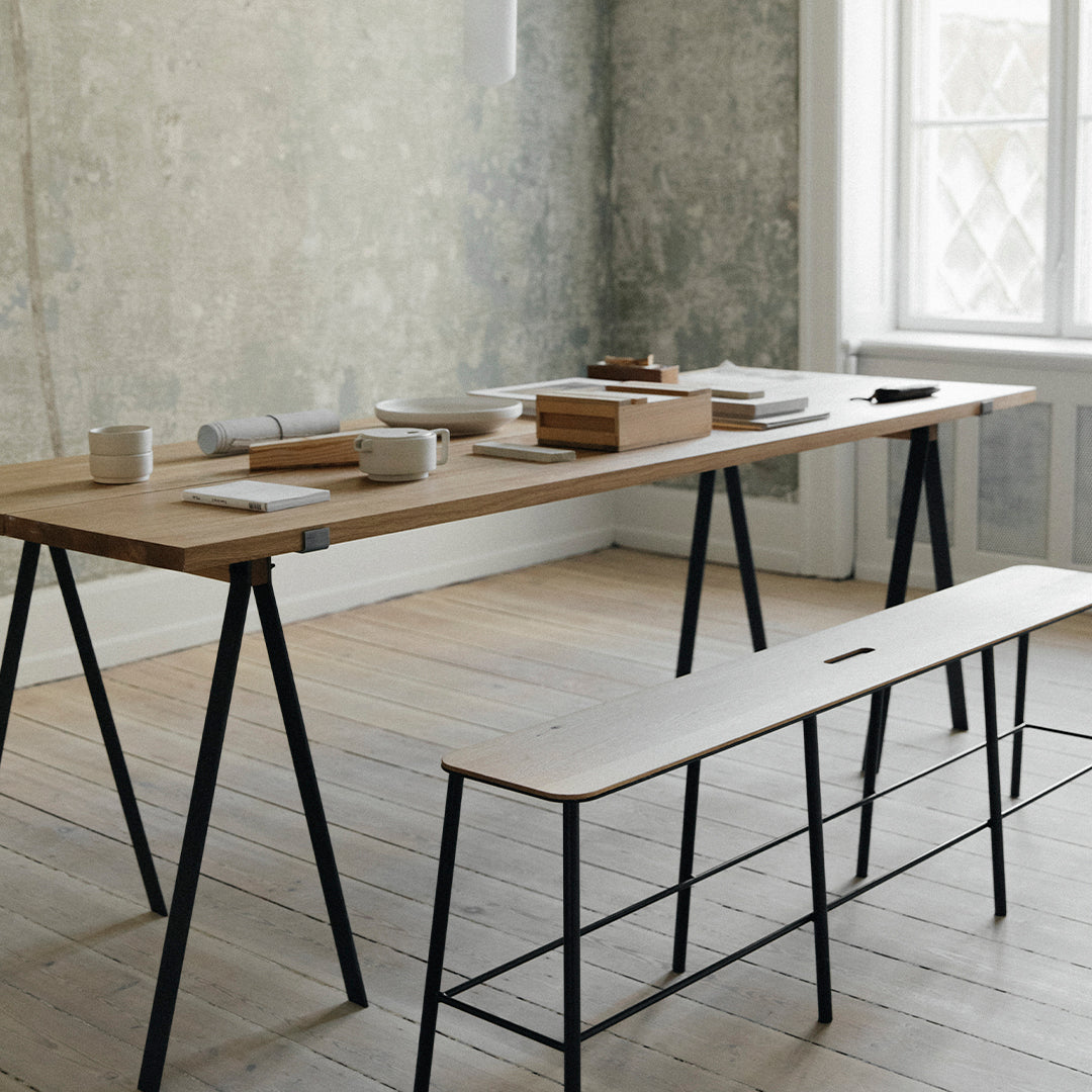 Minimalist wooden dining table with a light natural finish and black metal legs, complemented by a simple bench.