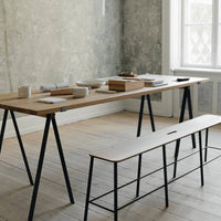 Minimalist wooden dining table with a light natural finish and black metal legs, complemented by a simple bench.