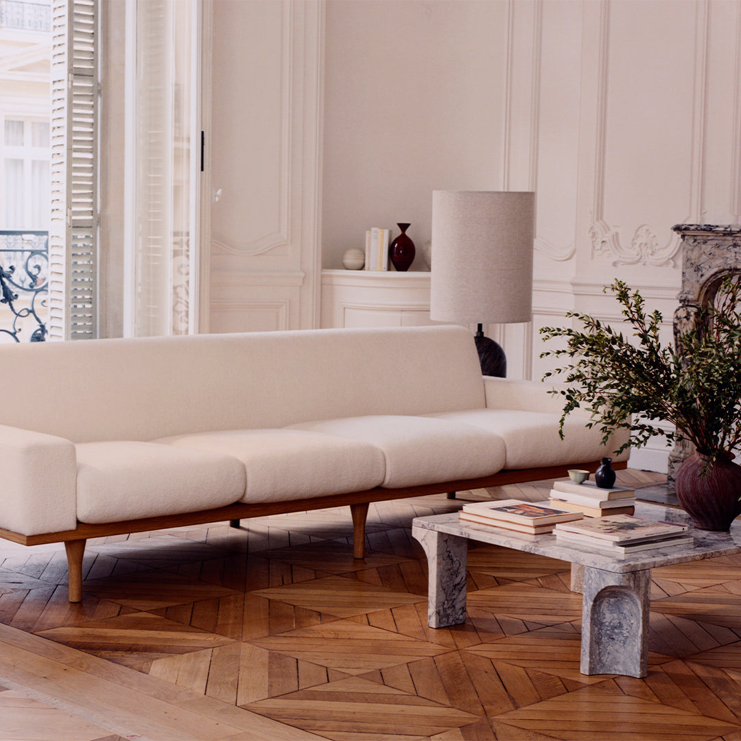 Modern cream sofa with wooden legs, paired with a textured gray coffee table, set on a warm herringbone wood floor.