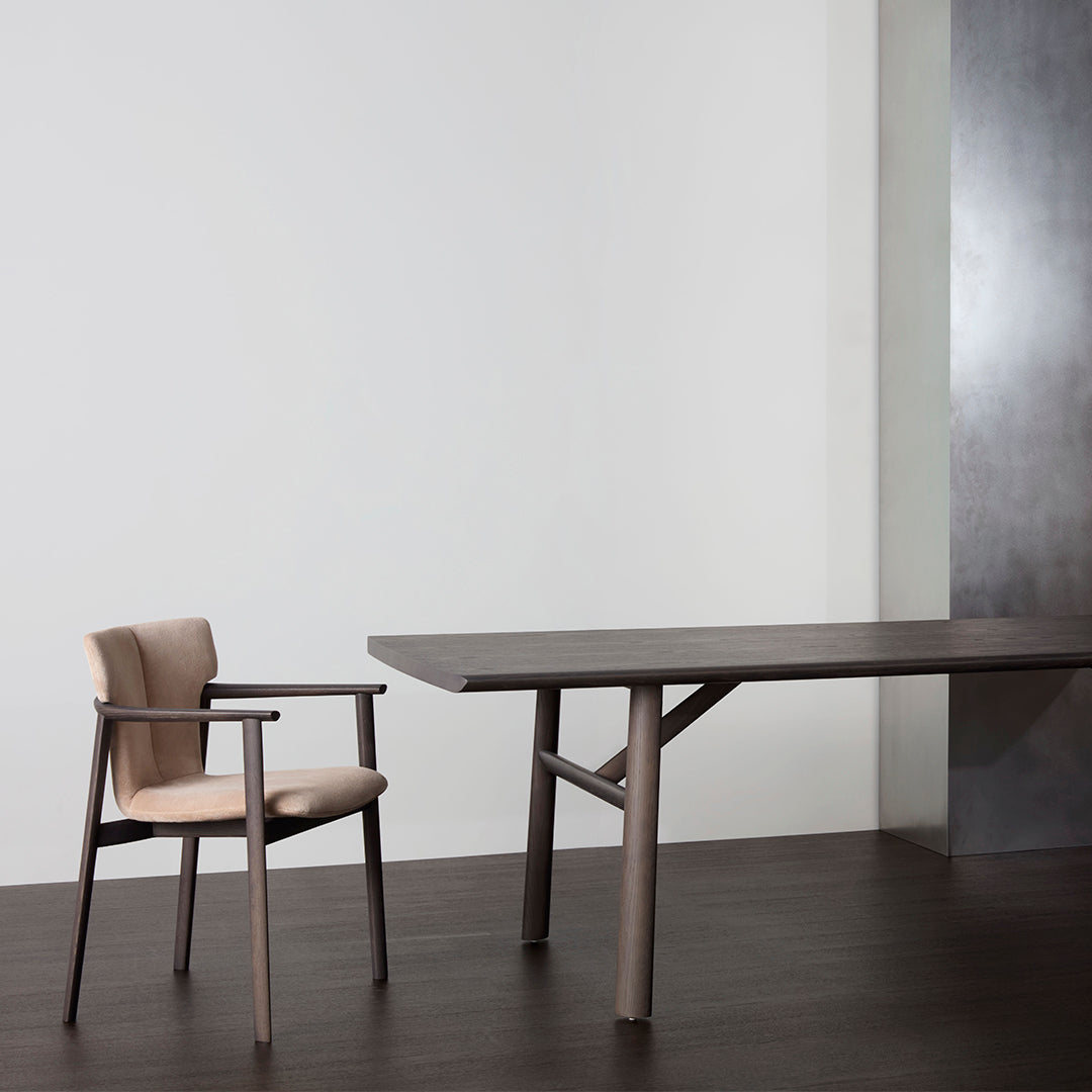 Elegant brown wooden table with a beige upholstered chair, set against a minimalist backdrop. Modern design, sleek lines.