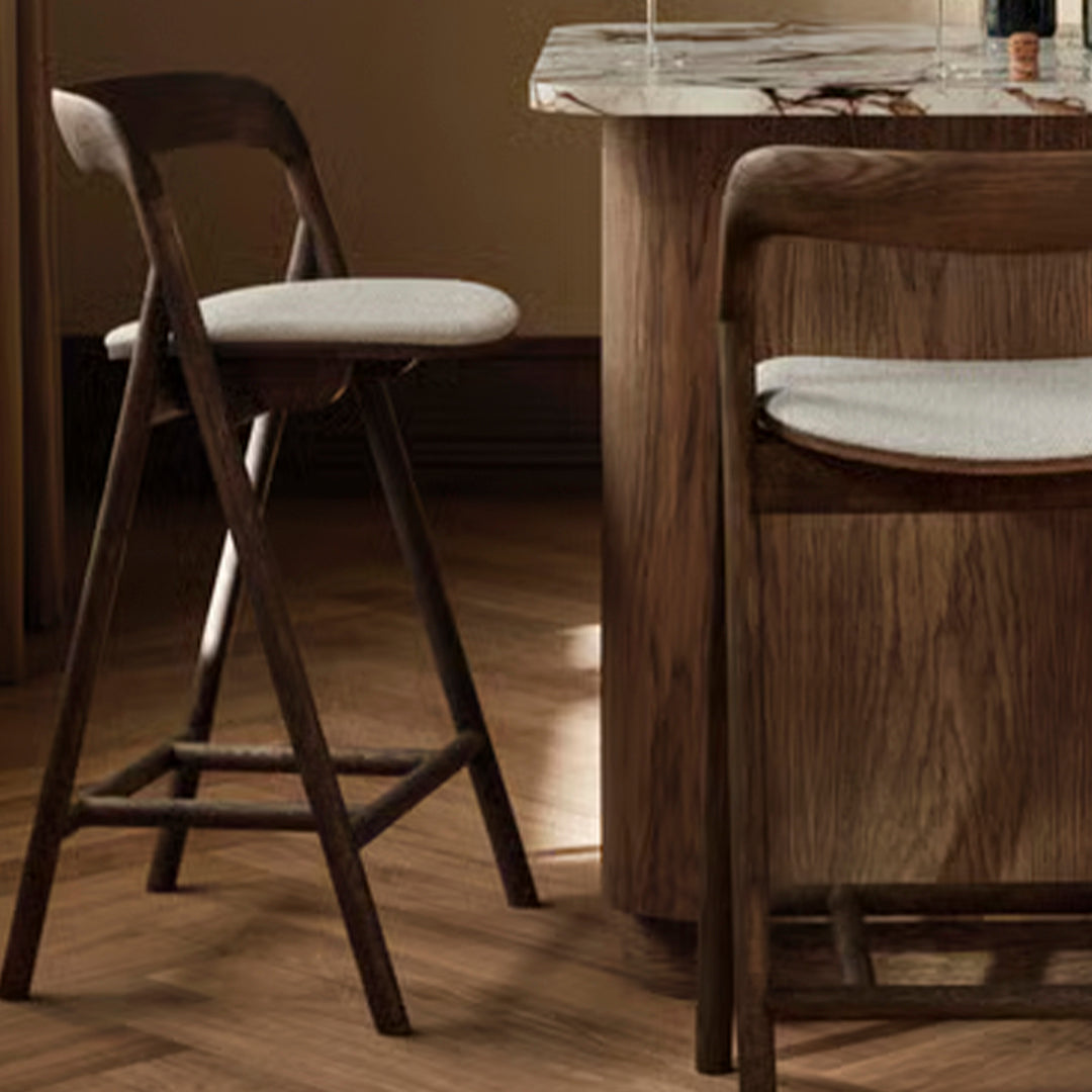 "Brown wooden bar stools with light gray cushions on a textured wooden floor."