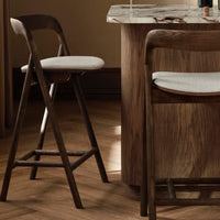 "Brown wooden bar stools with light gray cushions on a textured wooden floor."