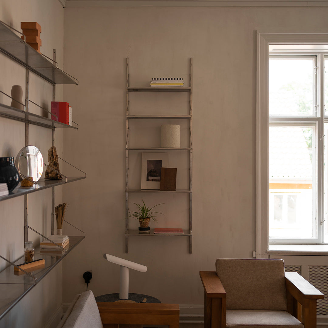 Stylish metal ladder bookshelf with a sleek silver finish against a soft beige wall, featuring minimalistic decor.