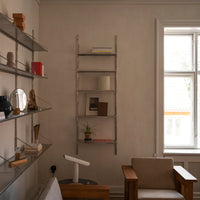 Stylish metal ladder bookshelf with a sleek silver finish against a soft beige wall, featuring minimalistic decor.