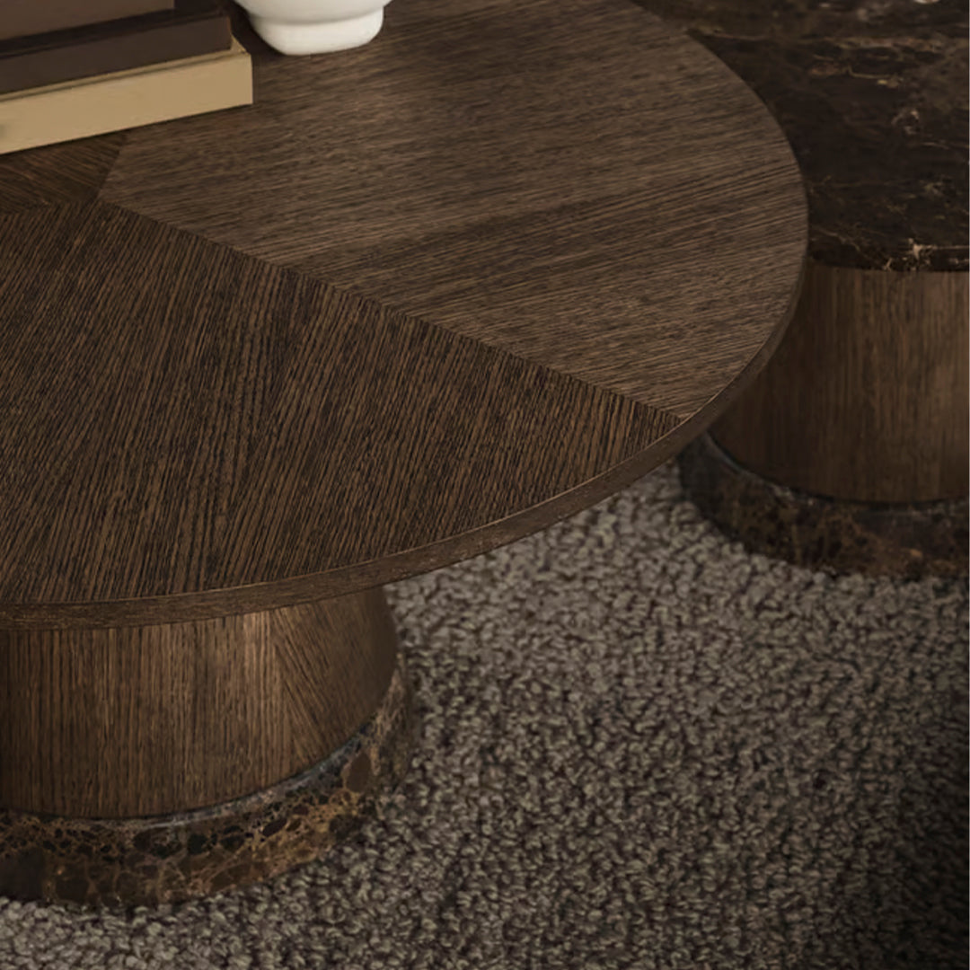 Brown round coffee table with textured wood grain pattern and dark circular base, set on a light, plush carpet.