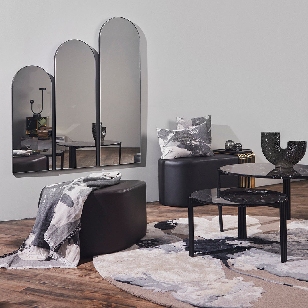Black and gray furniture with abstract patterns, featuring a soft beige rug and mirrored accents in a modern setting.