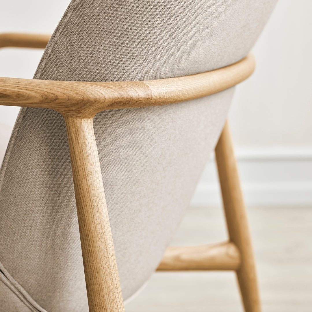 Light beige upholstered chair with a smooth, minimalist design and natural wooden frame. Perfect for modern decor.