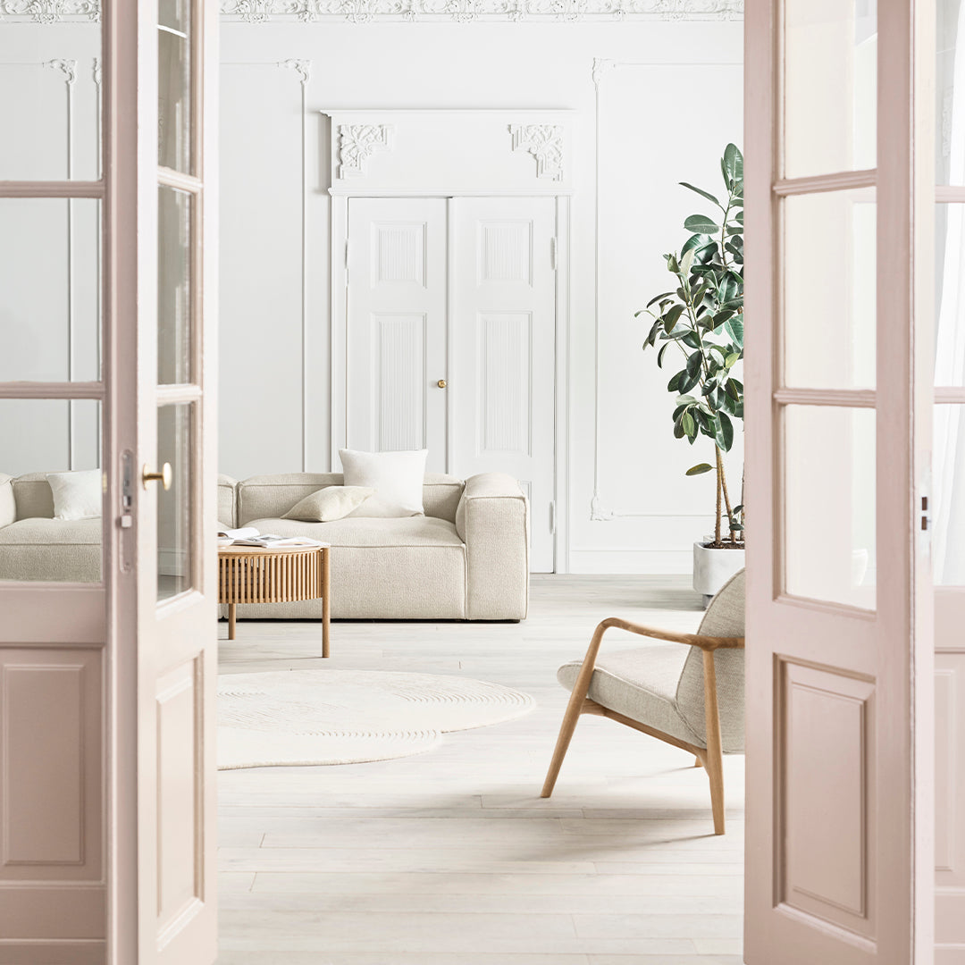 Light beige sofa and armchair in a minimalist, white-walled room with green plants and natural wood accents.