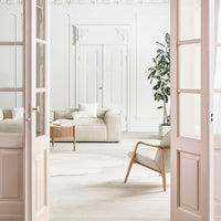 Light beige sofa and armchair in a minimalist, white-walled room with green plants and natural wood accents.