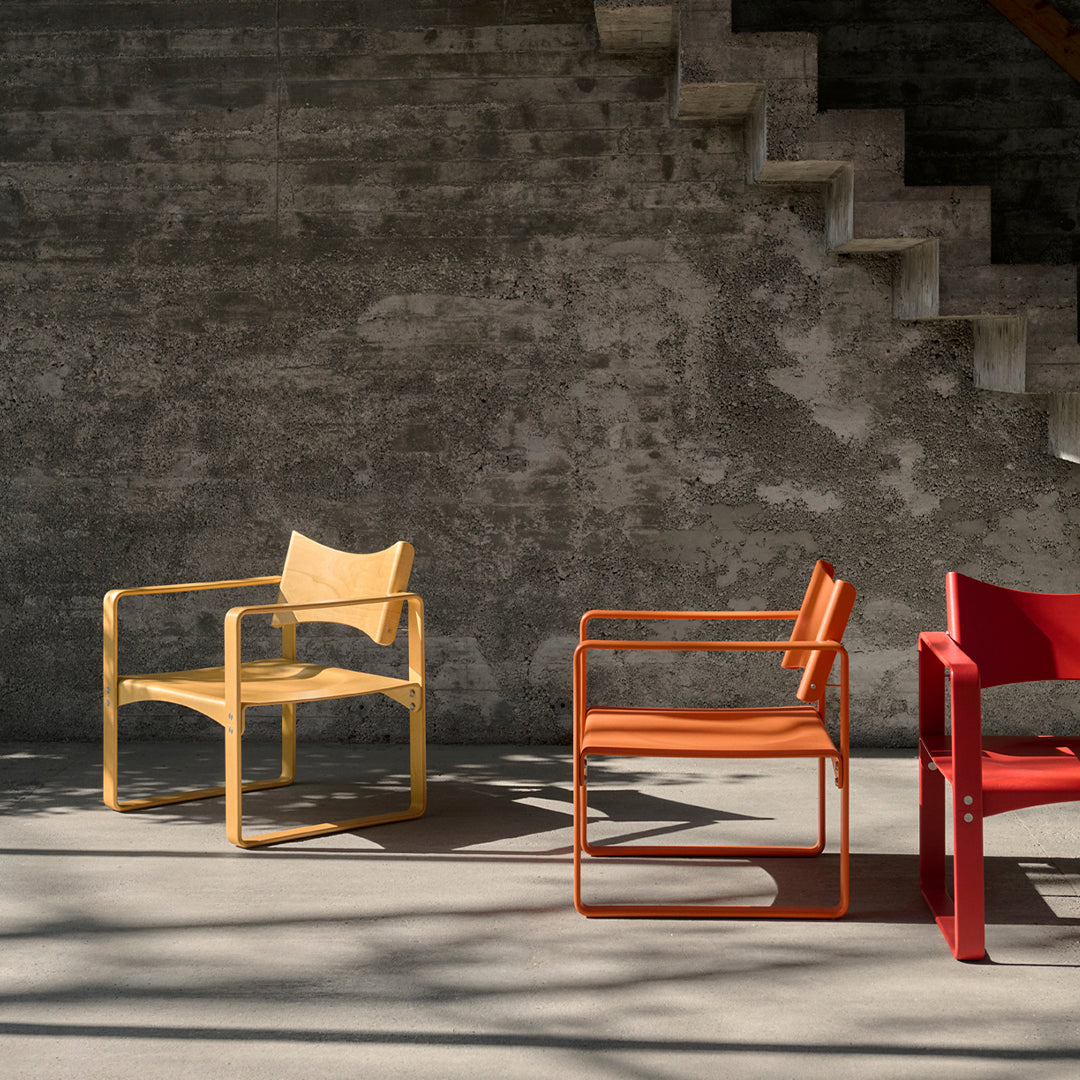 Three stylish chairs: a light yellow, vibrant orange, and bold red, against a textured gray background. Modern design.