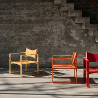 Three stylish chairs: a light yellow, vibrant orange, and bold red, against a textured gray background. Modern design.