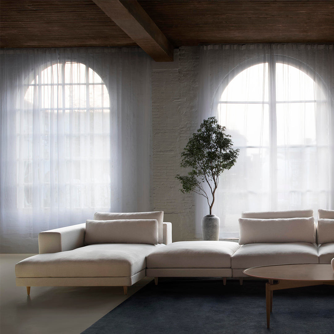 Neutral beige sectional sofa with soft white cushions, set against a light gray backdrop and dark blue area rug.