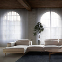 Neutral beige sectional sofa with soft white cushions, set against a light gray backdrop and dark blue area rug.