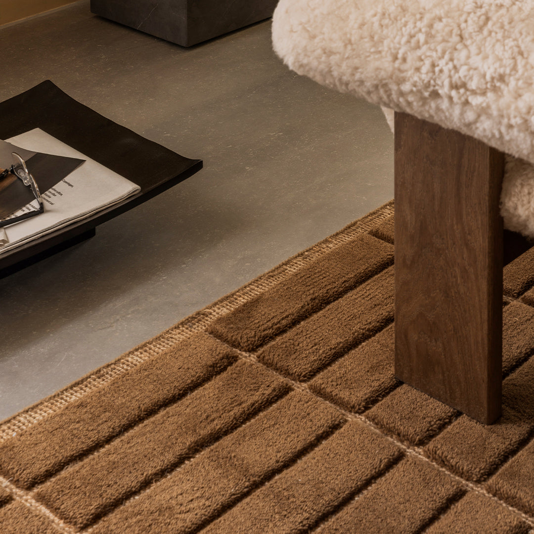 Brown textured rug with a striped pattern, placed under a chair in a modern living space.