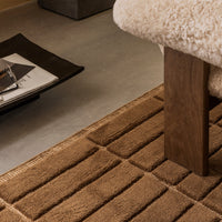 Brown textured rug with a striped pattern, placed under a chair in a modern living space.