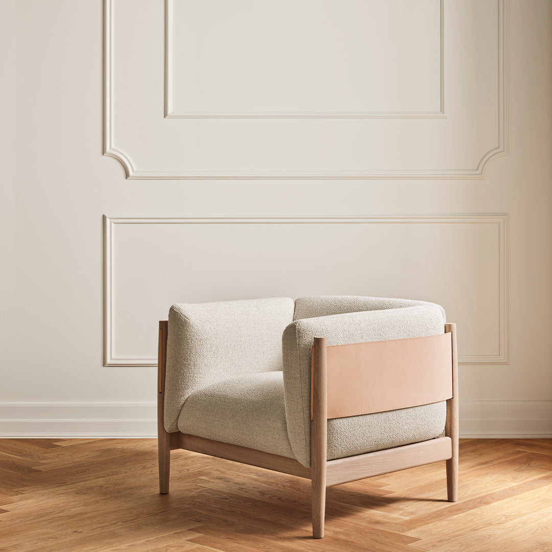 Light beige fabric armchair with a smooth, minimalist design and warm wood accents against a neutral backdrop.