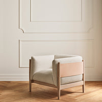 Light beige fabric armchair with a smooth, minimalist design and warm wood accents against a neutral backdrop.