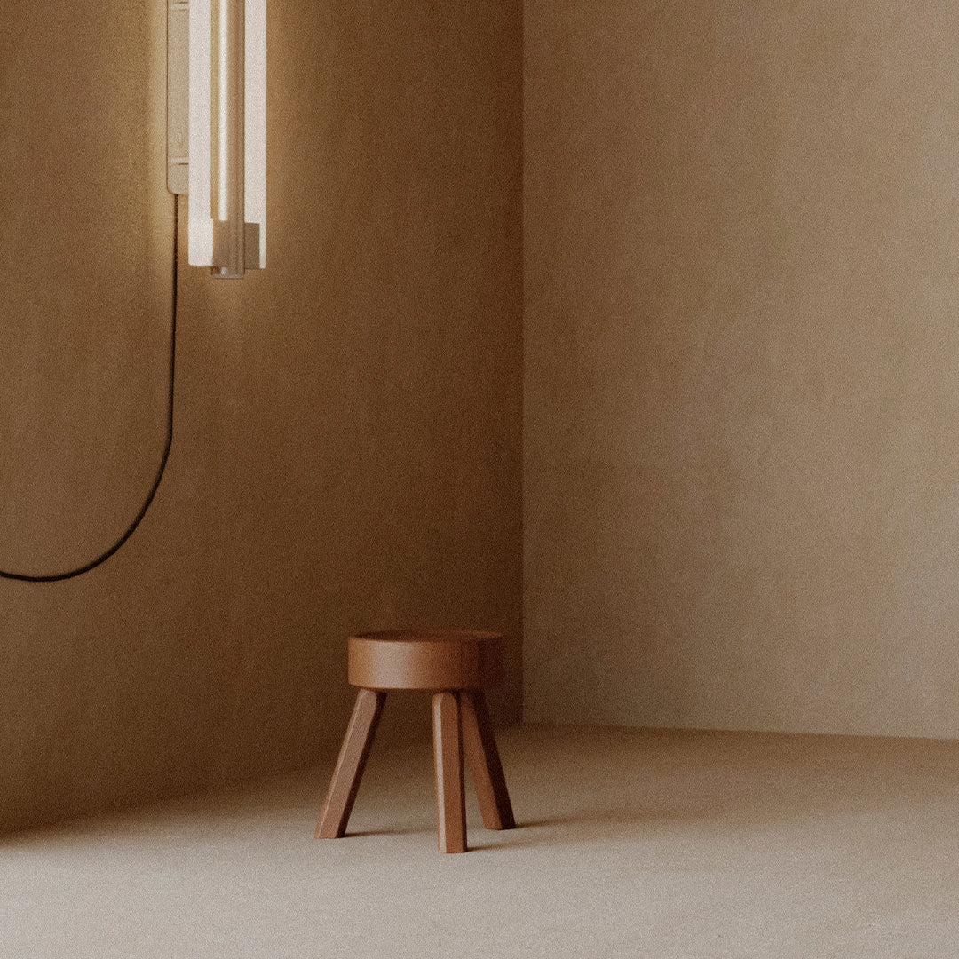 Rustic brown stool on beige floor with minimalist design and warm, soft lighting.