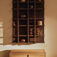 Dark wood shelving unit with geometric patterns and warm tones, showcasing decorative items against a neutral background.