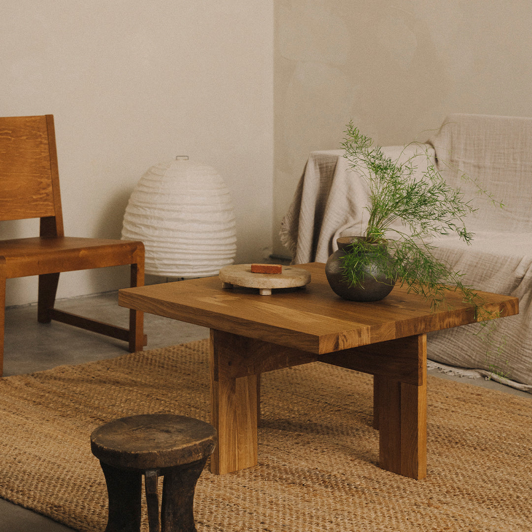 Wooden coffee table with a natural finish, circular patterned centerpiece, and green foliage accent in a neutral-toned room.