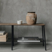 Wooden table with a natural finish, black metal legs, and a ceramic pot in earthy tones on a textured gray background.
