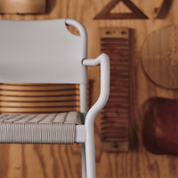 Light gray chair with textured woven pattern and smooth white armrests against a warm wooden background.