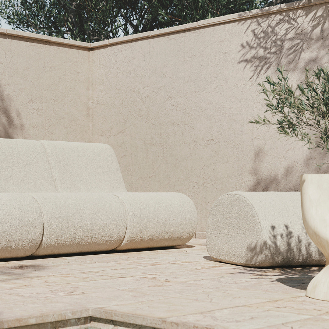 "Beige outdoor sofa with smooth, rounded patterns, complemented by a matching cylindrical ottoman."
