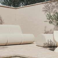 "Beige outdoor sofa with smooth, rounded patterns, complemented by a matching cylindrical ottoman."