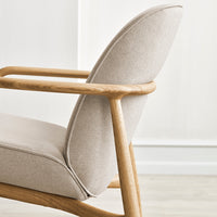 Light beige fabric armchair with a smooth, curved design and natural wood accents. Soft, elegant color palette.