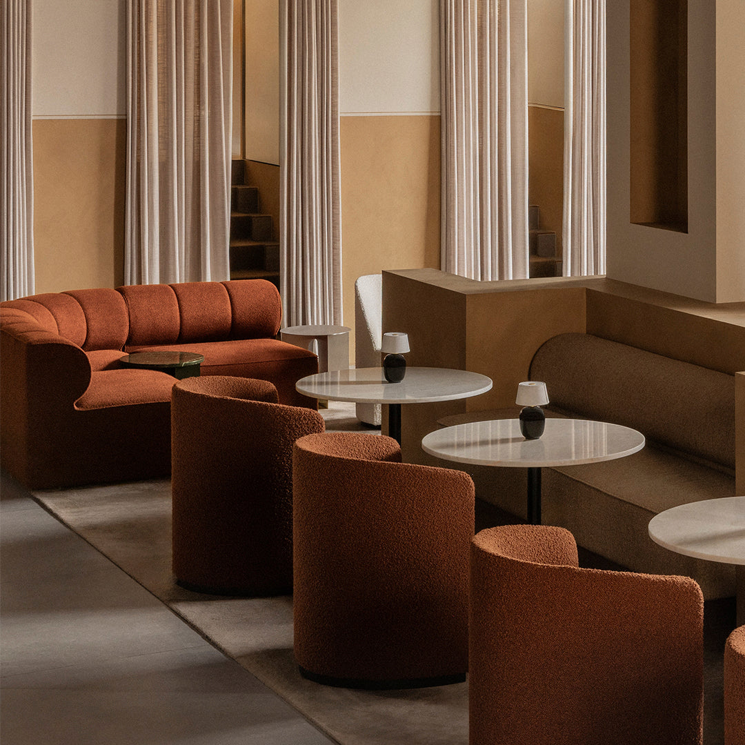 Warm terracotta upholstery with soft, rounded shapes and neutral beige accents, complemented by minimalist white tables.