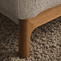 Textured gray fabric with warm wood leg against a neutral woven rug, showcasing a cozy, natural color palette.