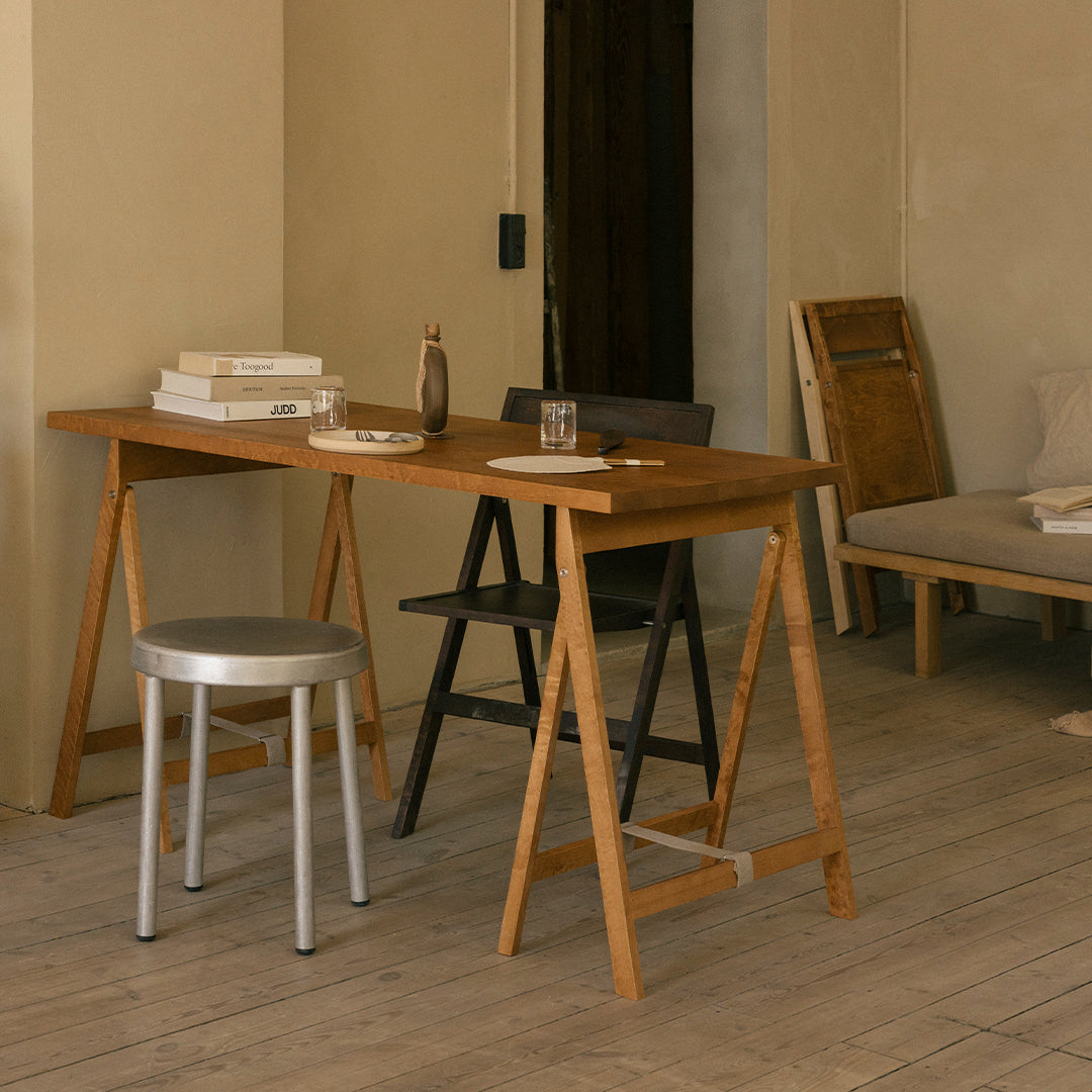 Light wooden desk with natural finish, complemented by a silver metal chair, set in a neutral-toned interior.