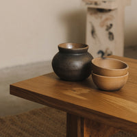Ceramic bowls in earthy tones of black and beige, featuring smooth finishes and subtle textures on a wooden table.