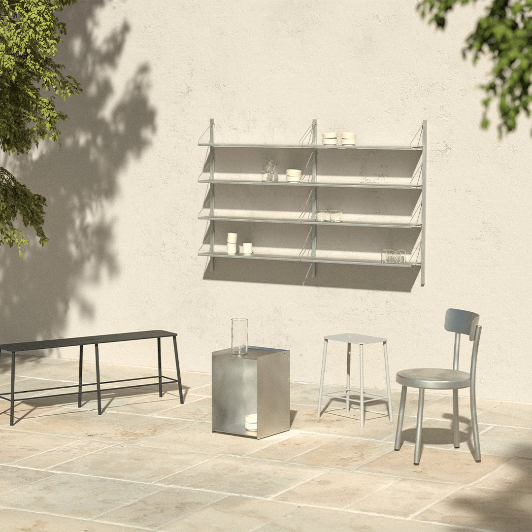 Minimalist gray furniture set against a light, textured wall with soft shadows and greenery in the background.