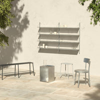 Minimalist gray furniture set against a light, textured wall with soft shadows and greenery in the background.