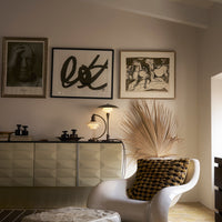 Stylish white chair with black and yellow checkered cushion, modern art prints, and neutral tones in the decor.