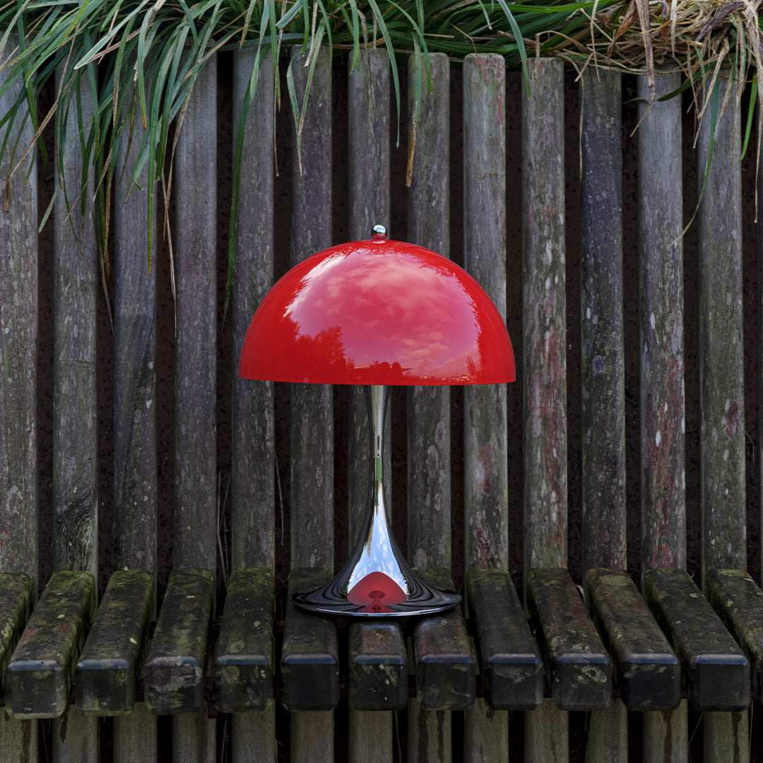 Glossy red lamp with a sleek chrome base, set against rustic wooden slats and greenery. Perfect for modern decor.